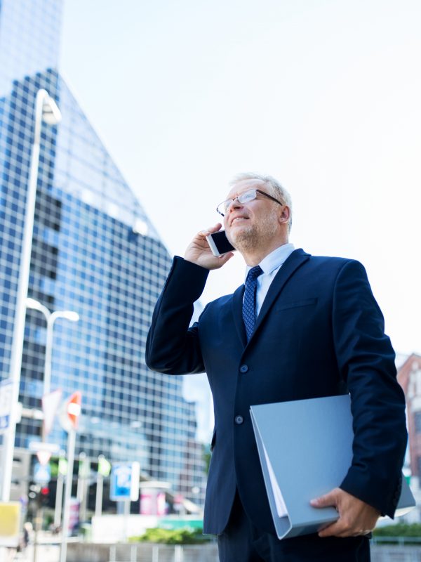 business, technology, communication and people concept - senior businessman with document folder calling on smartphone in city